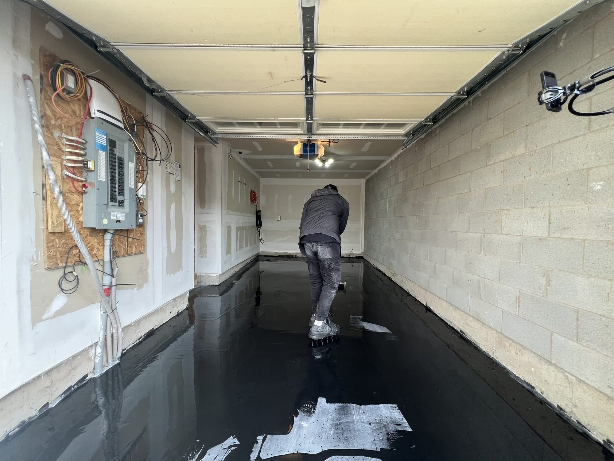 Black epoxy resin flooding a garage floor, still wet and mirror-like