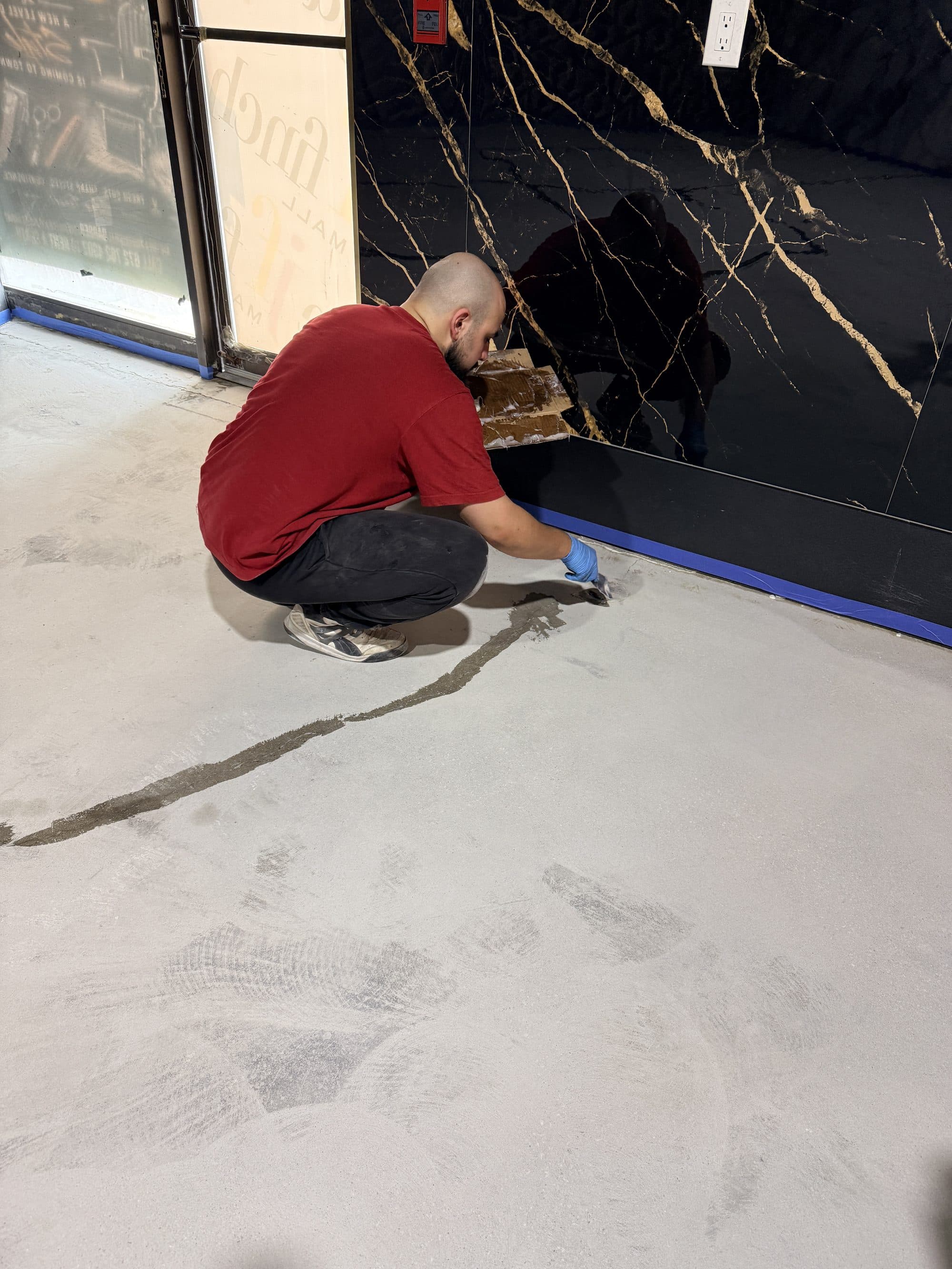 An installer cutting a clean epoxy edge against a dark feature wall in a showroom