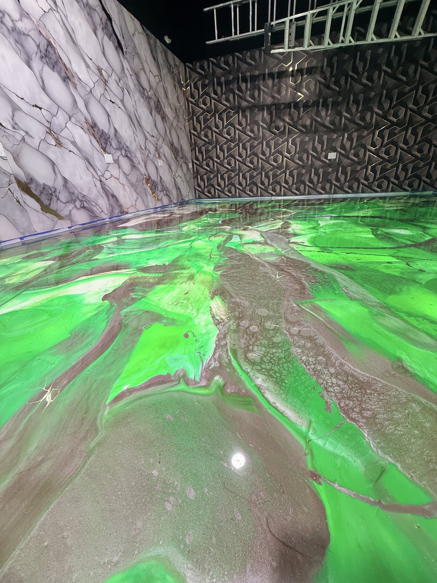 A finished emerald green metallic epoxy floor in a marble-clad commercial showroom