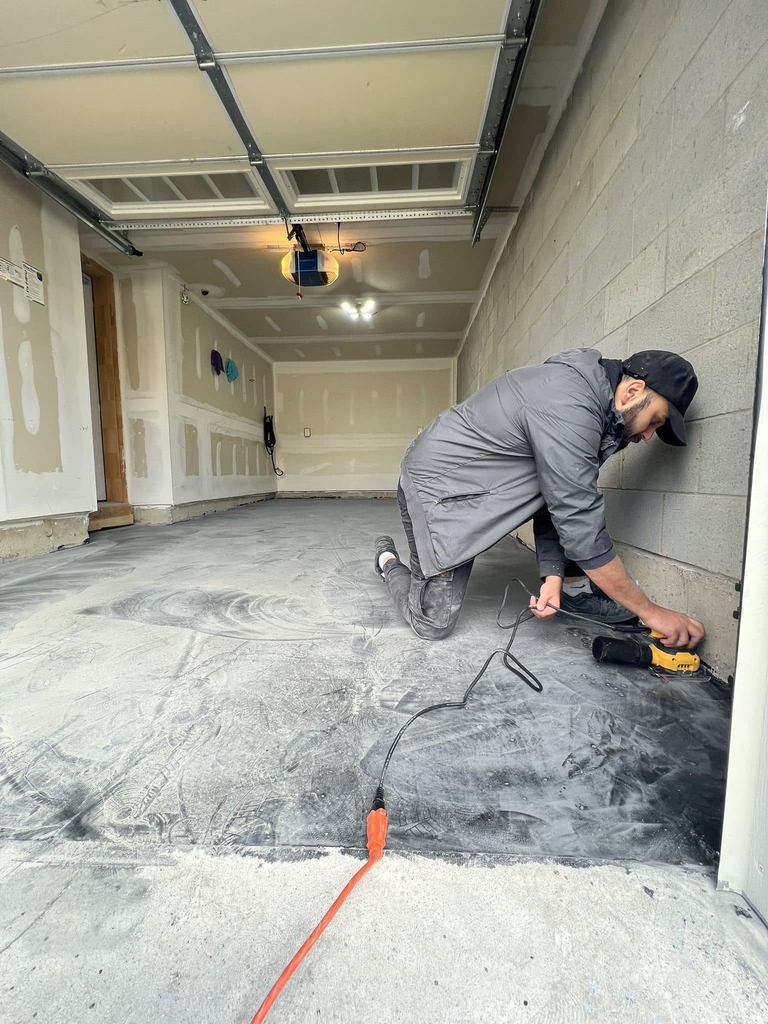 An installer kneeling to fill a crack in a garage slab by hand before resin is poured