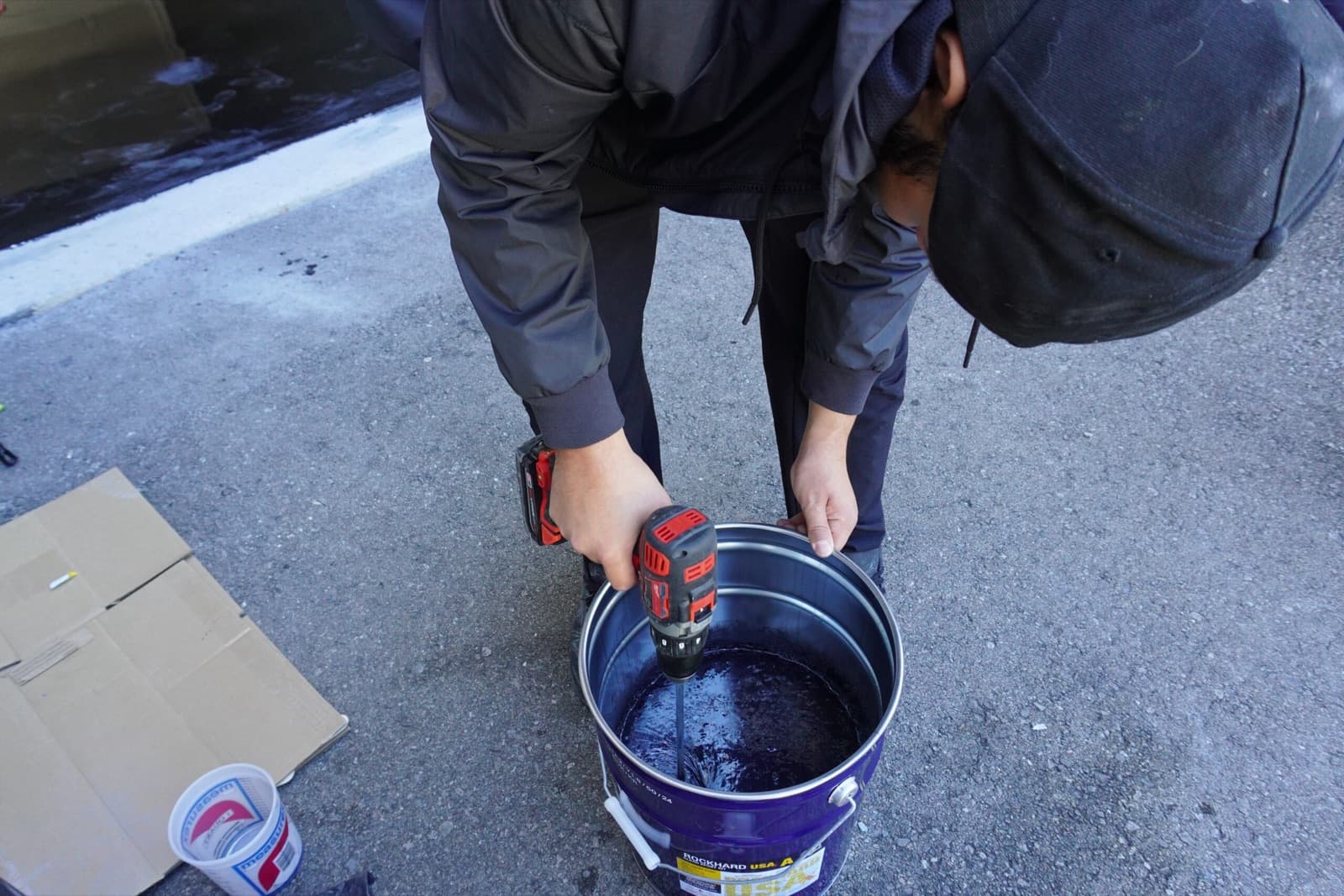 An installer drill-mixing a batch of epoxy resin in a bucket on the driveway