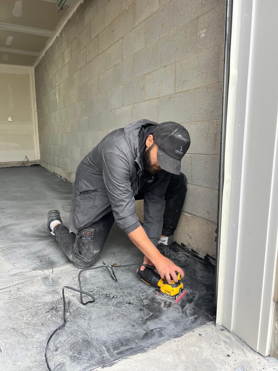 An installer cutting a clean epoxy edge along the wall line of a garage