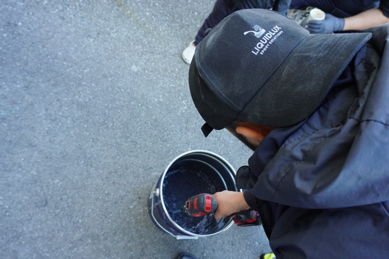 An installer power-mixing pigmented epoxy resin in a bucket on the job site