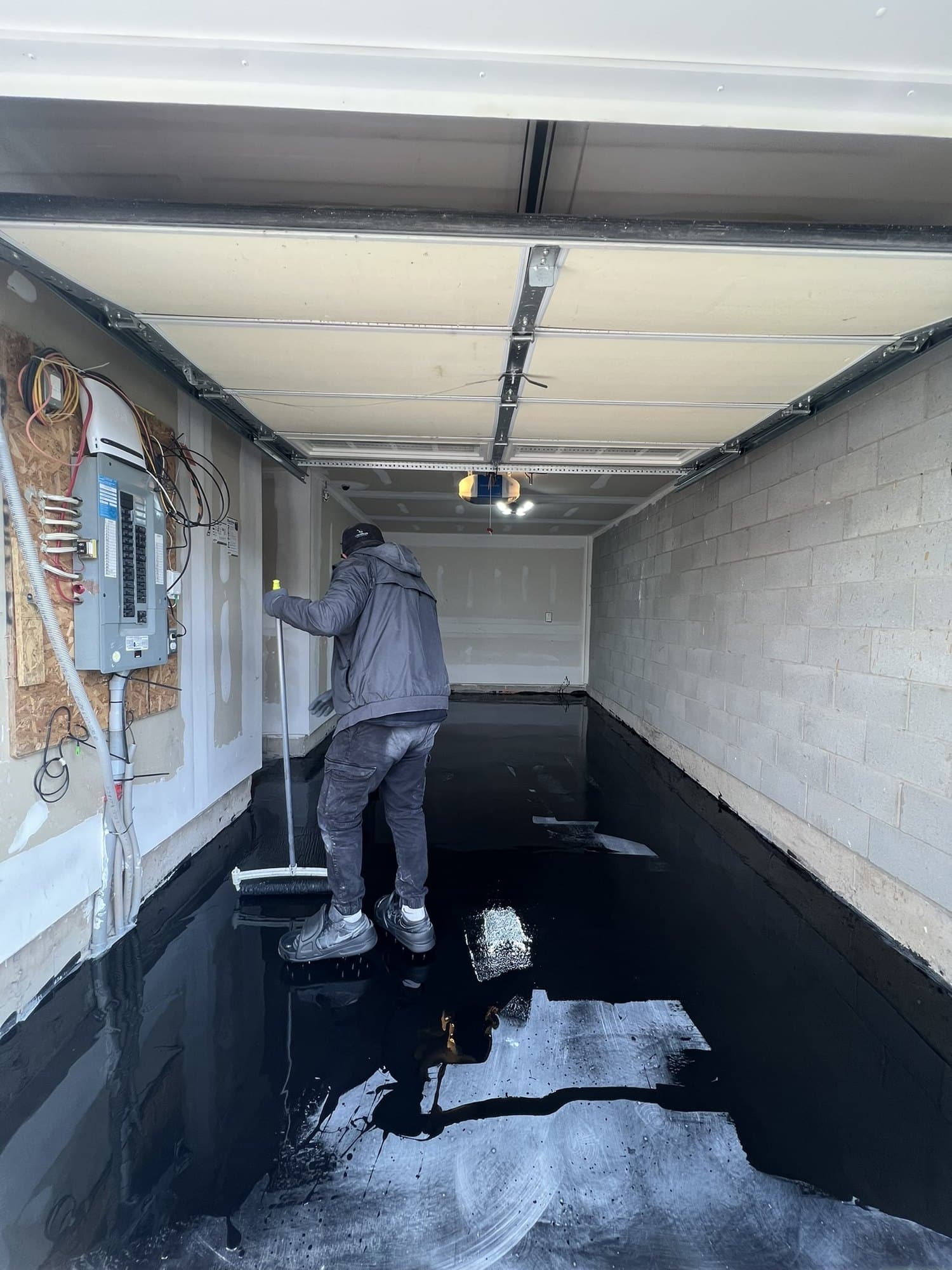 A poured epoxy floor with a mirror-like black surface reflecting the garage ceiling