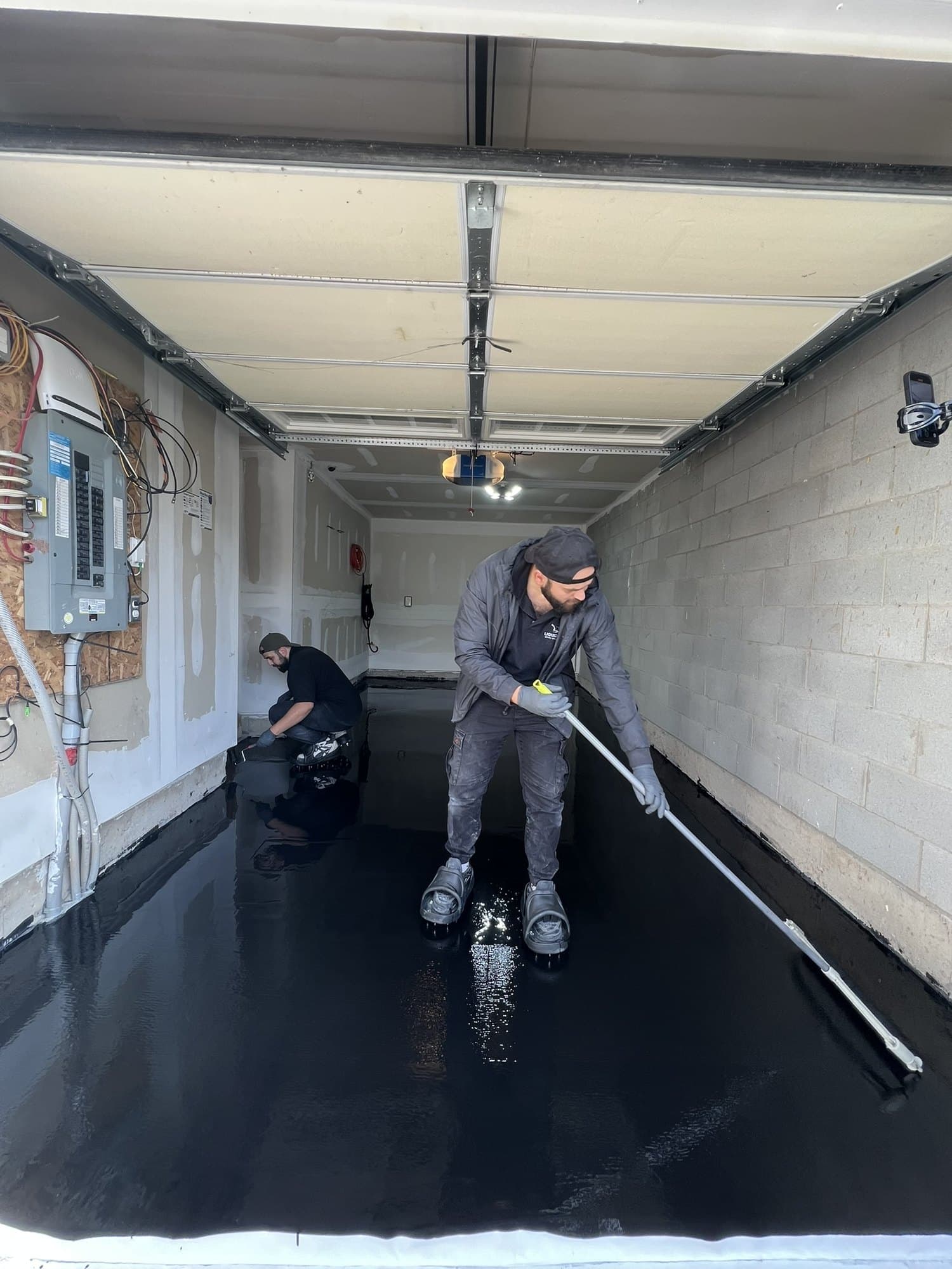 An installer pulling a squeegee across a wet mirror-black epoxy floor
