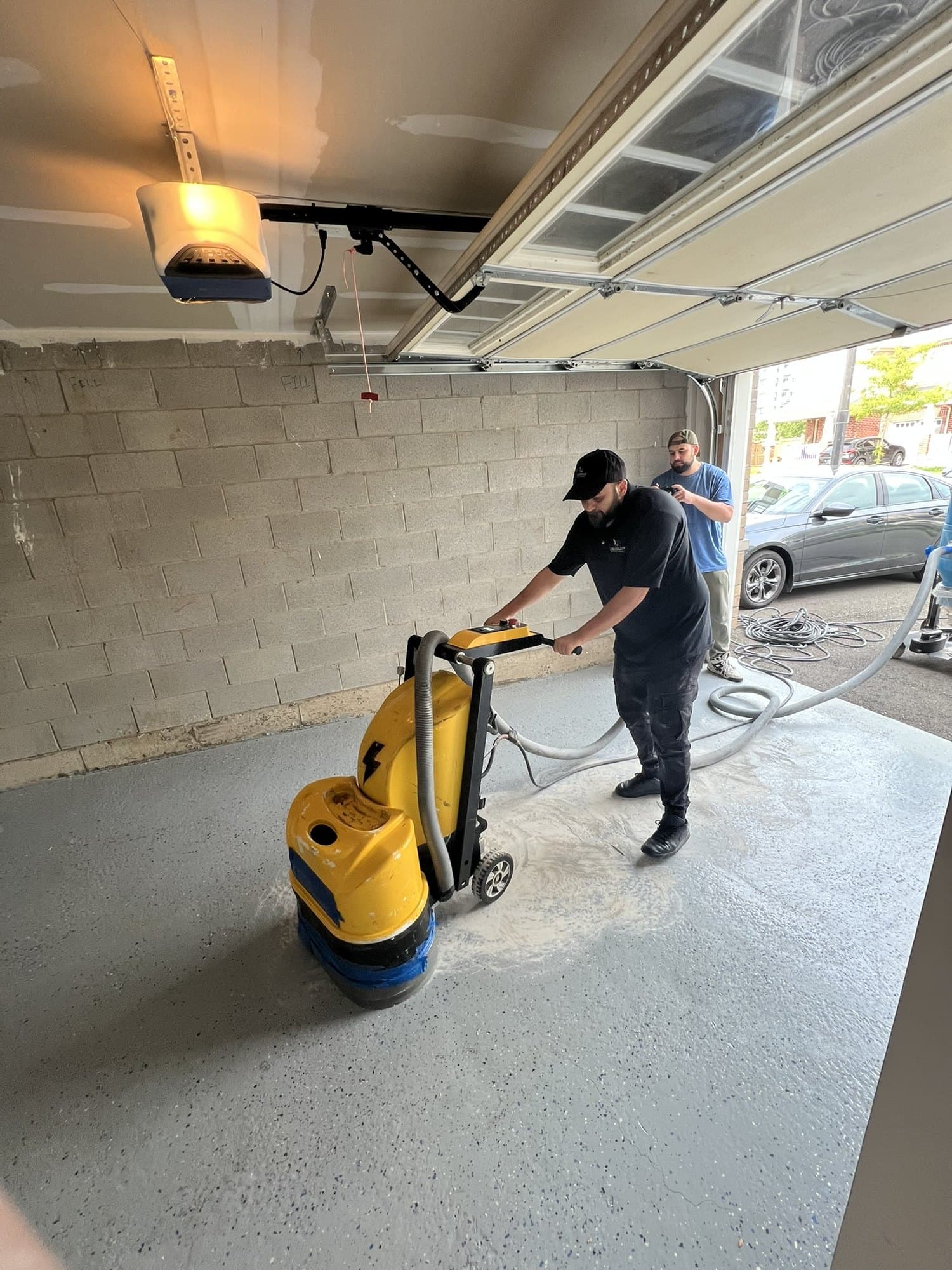 An installer diamond-grinding a garage slab back to bare concrete with a floor grinder